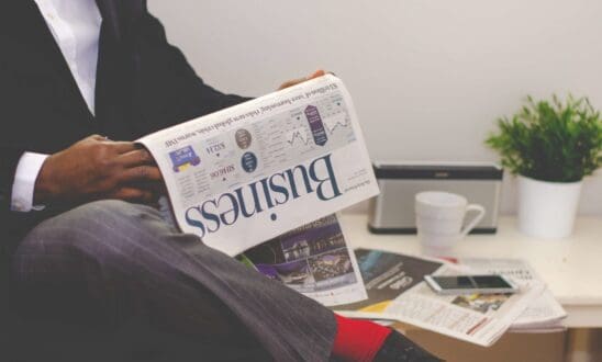 Black man with legs crossed reads the busines section of a newspaper