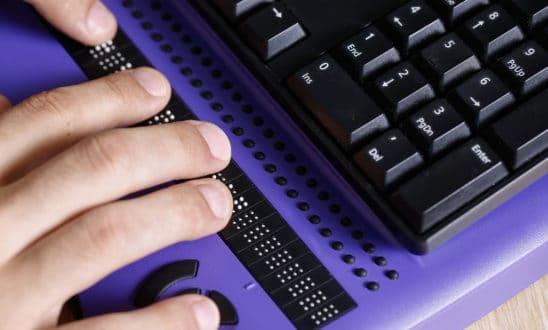 Blind person using computer with braille computer display and a computer keyboard.