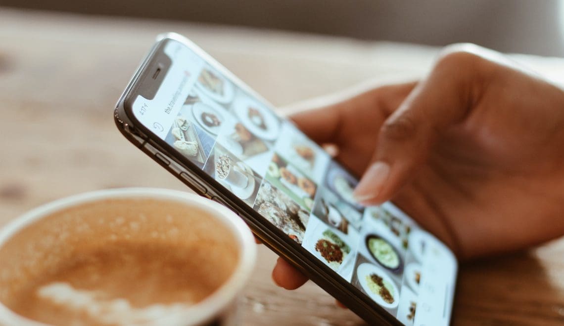 Close-up of a hand scrolling through Instagram with a latte in the background