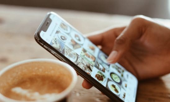Close-up of a hand scrolling through Instagram with a latte in the background