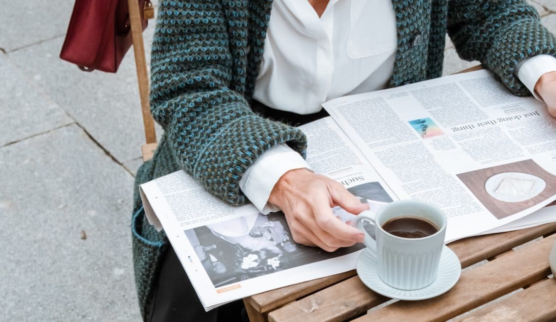 Woman reading a newspaper outside with a cup of black coffee