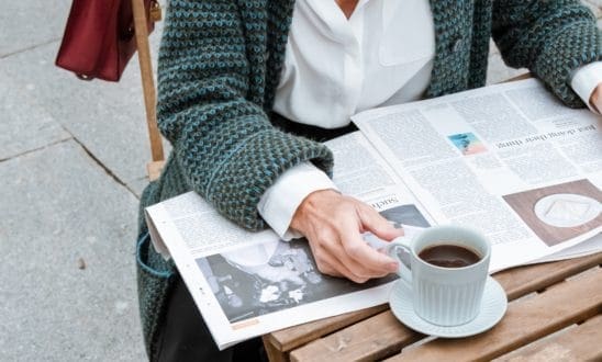 Woman reading a newspaper outside with a cup of black coffee