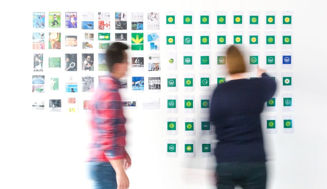 Two people in blurred motion stand in front of a wall of photos