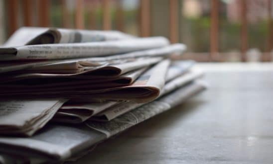 A stack of newspapers sit on a wooden table