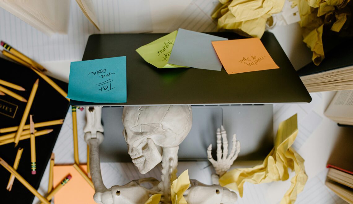 Skeleton laying down on a laptop covered in sticky notes